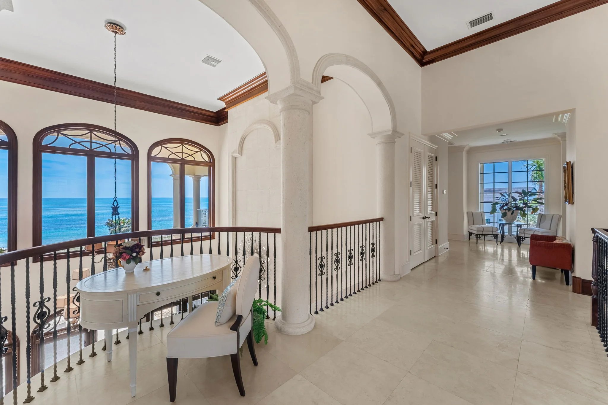 Upper landing with double archway, stone columns, secretary desk, and arched ocean windows