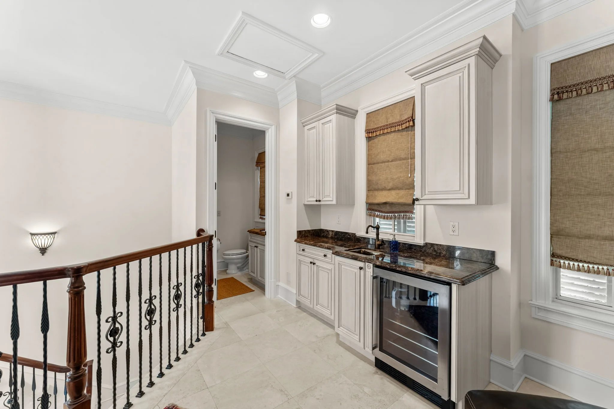 Upstairs landing wet bar with marble counter, wine fridge and arched iron stair rail